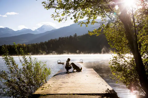 Photo of Young woman and dog watching sunrise by the lake.