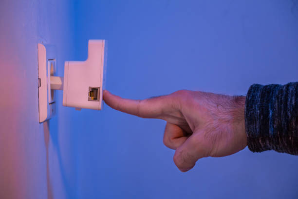 istock Man press with his finger on button on WiFi repeater which is in electrical socket on the wall 907870224