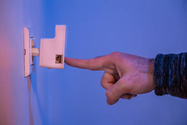 istock Man press with his finger on button on WiFi repeater which is in electrical socket on the wall 907870538