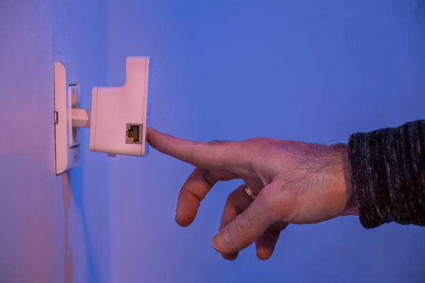 istock Man press with his finger on button on WiFi repeater which is in electrical socket on the wall 907871170