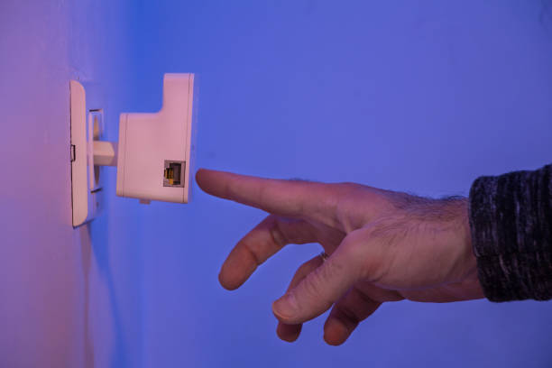 istock Man press with his finger on button on WiFi repeater which is in electrical socket on the wall 907871832