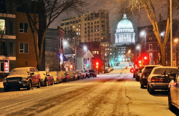 Beautiful night cityscape. Madison, the capitol of Wisconsin downtown street view with parked cars and Wisconsin state capitol building glowing in the snowy night. Wisconsin state, Midwest USA.