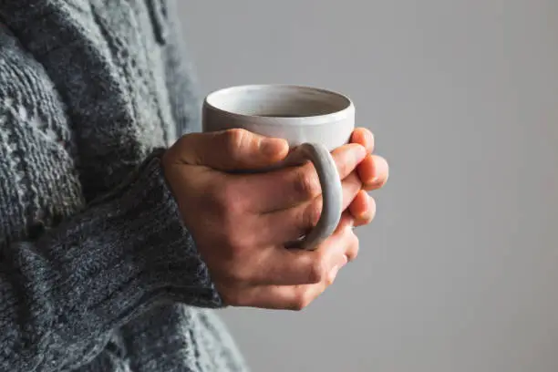 Photo of Woman in woolly gray sweater holding warm cup of tea