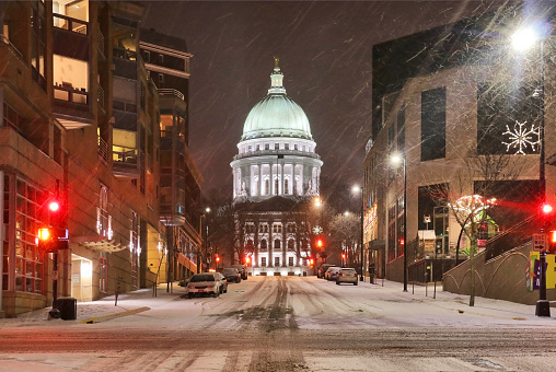 Beautiful night cityscape. Madison, the capitol of Wisconsin downtown street view with parked cars and Wisconsin state capitol building glowing in the snowy night. Wisconsin state, Midwest USA.