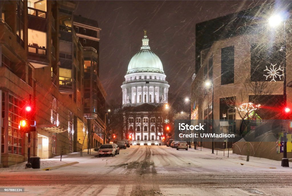 American town architecture and city life background. Beautiful night cityscape. Madison, the capitol of Wisconsin downtown street view with parked cars and Wisconsin state capitol building glowing in the snowy night. Wisconsin state, Midwest USA. Madison - Wisconsin Stock Photo