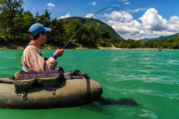 Fly fisherman on bellyboat fighting with big trout, Slovenia Fisherman sitting in bellyboat and fighting with big trout on lake in Jesenice, Slovenia. Still water fly fishing and outdoor lifestyle theme. municipality of jesenice photos stock pictures, royalty-free photos & images