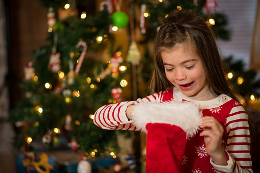 Little girl opening her presents in front of the tree on Christmas morning