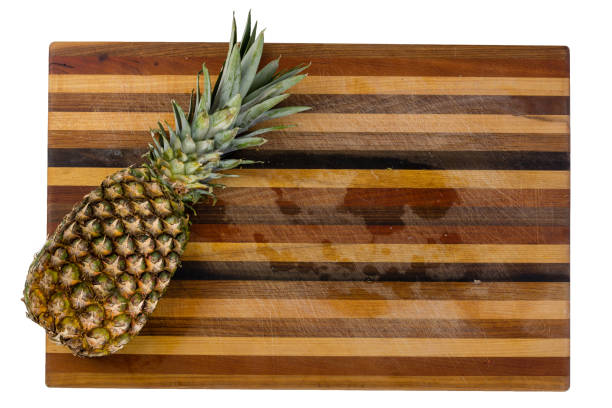Ripe whole tropical pineapple on an ornament striped wooden cutting board with copy space isolated on white viewed from overhead