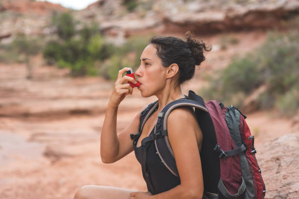 Woman With Chronic Asthma Hiking in Desert A young ethnic female takes a short break from her day hike in the Utah desert to use her inhaler. asthma inhaler stock pictures, royalty-free photos & images