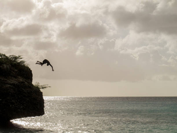 istock Man jumps off cliff into Caribbean Sea 907907740