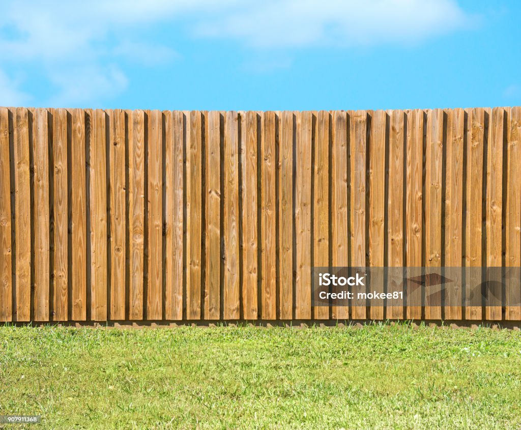 Generic wooden residential privacy fence with green grass yard Generic wooden residential privacy fence with  a lush green grass yard in the foreground and a beautiful blue sky with fluffy clouds. Fence Stock Photo