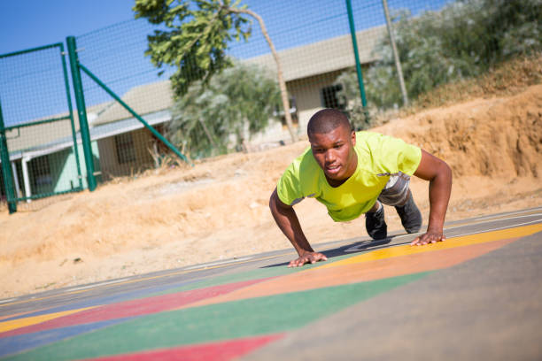 Burpees outside at the playground A black male does some burpees as part of his training regime outside on a court burpee stock pictures, royalty-free photos & images