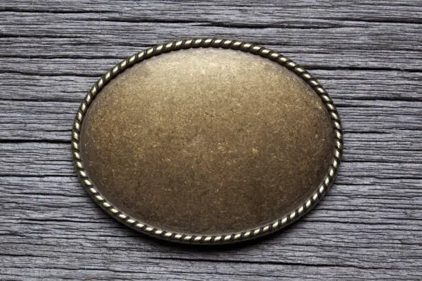 An oval shaped belt buckle resting on top of a gray weathered wood surface.