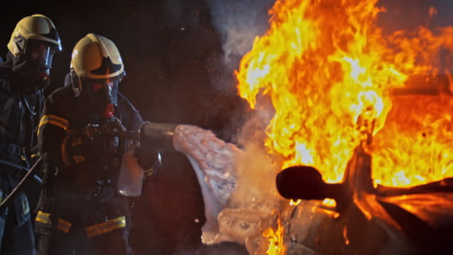 SLO MO Firefighters spraying foam onto a burning vehicle at night