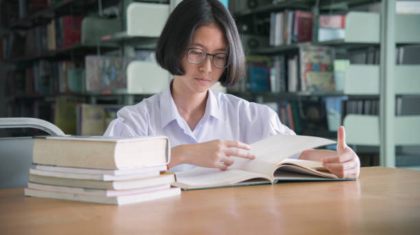 istock Asian student girl reading book in public library 907921130