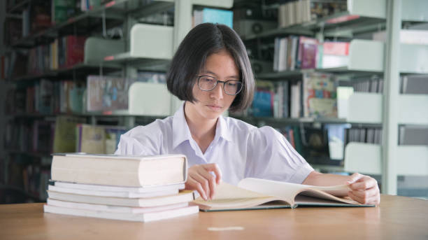 istock Asian student girl reading book in public library 907921148