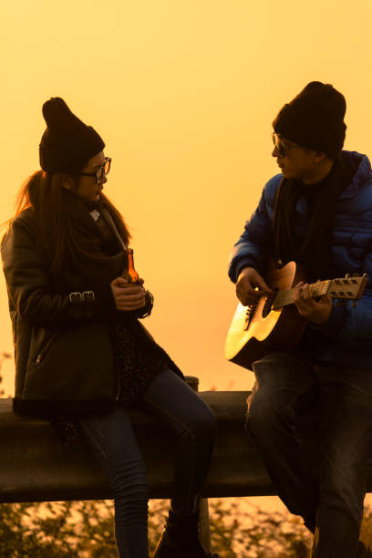 junges paar am strand, mann spielt gitarre - face to face twilight togetherness vertical stock-fotos und bilder