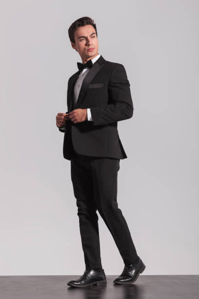 istock walking young man buttoning his tuxedo and looks to side 907928742