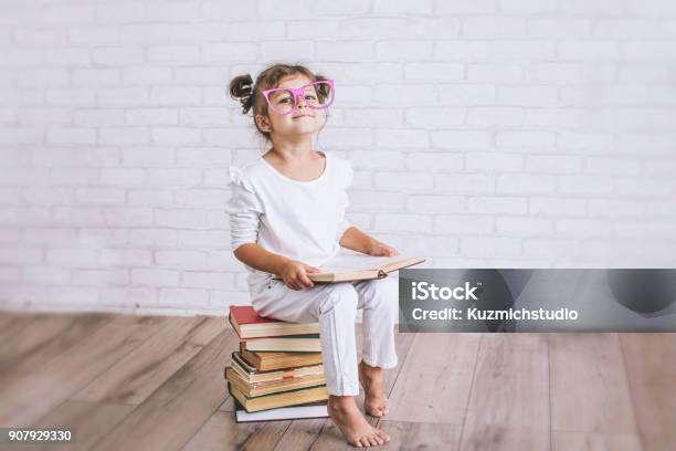 Child Little Girl Sitting On A Stack Of Books With Glasses Stock Photo - Download Image Now