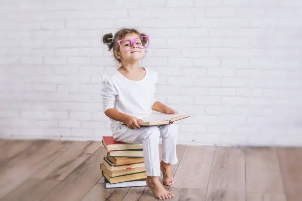 Photo of Child little girl sitting on a stack of books with glasses