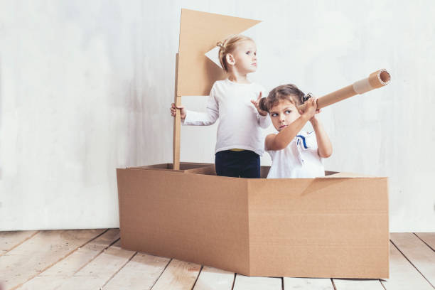 zwei kinder spielen kleine mädchen nach hause in einem karton schiff, kapitäne und matrosen - child playground small toy stock-fotos und bilder