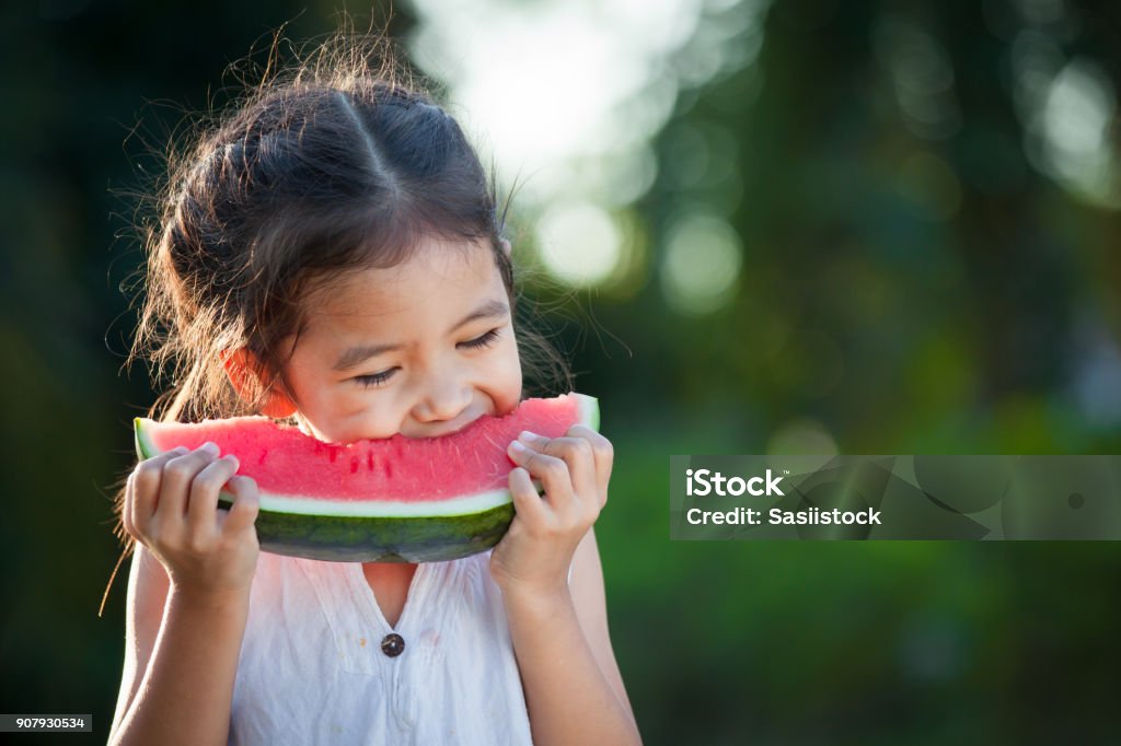 Asia infantil niña linda comer fruta fresca de sandía en el jardín - Foto de stock de Niño libre de derechos