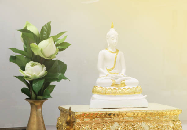 istock White Buddha with light effects  on wood table gold color 907933290