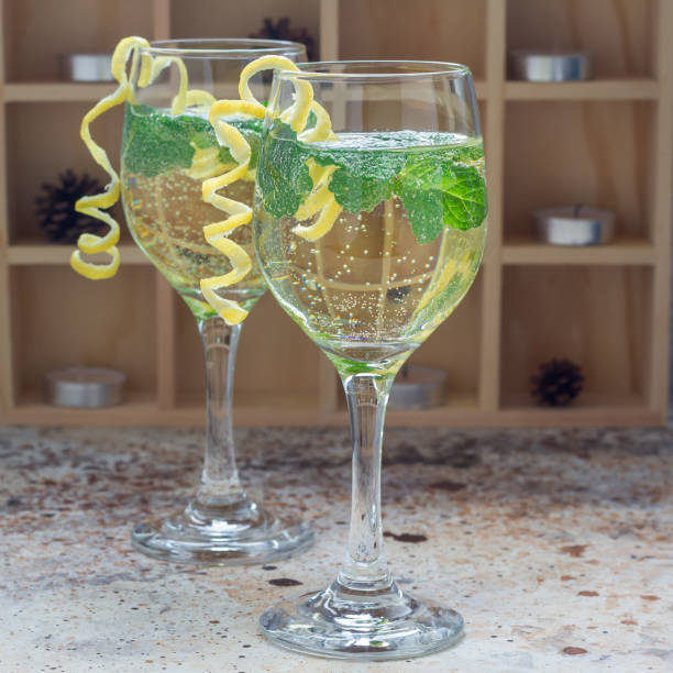 Spritzer cocktail with white wine, mint and ice, decorated with spiral lemon zest, square
