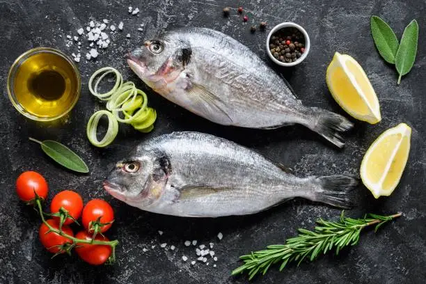 Photo of Fresh sea fish Dorado or Sea Bream with herbs and spices on slate background ready for cooking