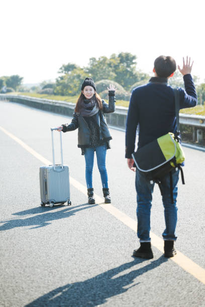 istock girlfriend pulling wheeled luggage waving goodbye to her boydriend 907935446