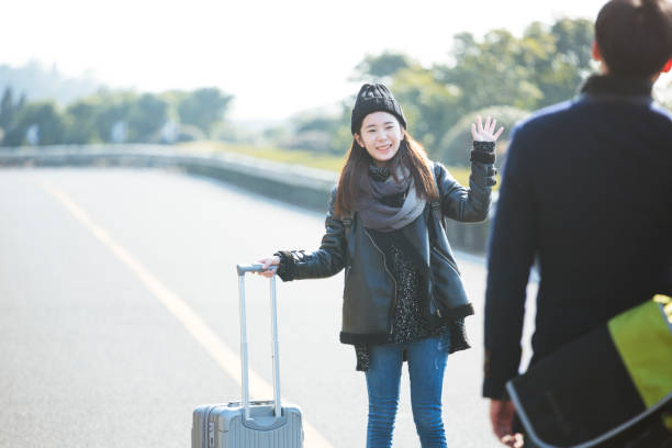 istock girlfriend pulling wheeled luggage waving goodbye to her boydriend 907935526