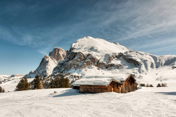 Two small wooden log cabin on meadow Alpe di Siusi on sunrise time. Seiser Alm, Dolomites, Italy. Snowy hills with orange larch and Sassolungo and Langkofel mountains group. Landscape photography