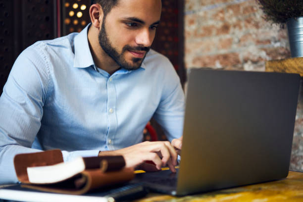 istock Concentrated handsome male businessman working via laptop computer checking email box waiting for receiving report, pensive freelancer creating advertising content earning money online sitting in cafe 907937334