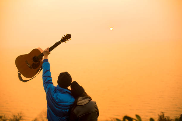 young couple with guitar standing at the hillside,rear view,China.