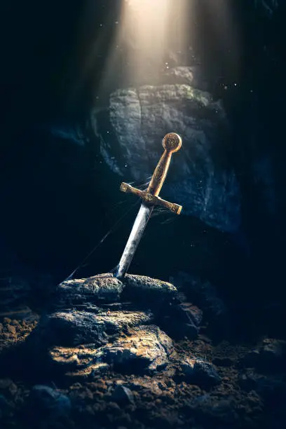 High contrast image of Excalibur, sword in the stone with light rays and dust specs in a dark cave
