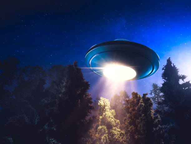 istock High contrast image of UFO flying over a forest with light beam at night 907940772