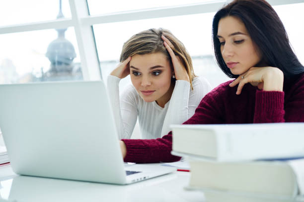 istock Tired blonde student watching webinar together with friend on laptop computer device connecting to wireless high speed 4G internet.Concentrated young women studying at modern technology in college 907941814