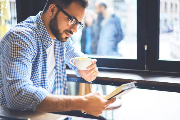istock Confident casually dressed graphic designer thinking about improving strategy planning for new project checking notes, handsome student in eyewear analyzing information creating coursework in cafe 907942110