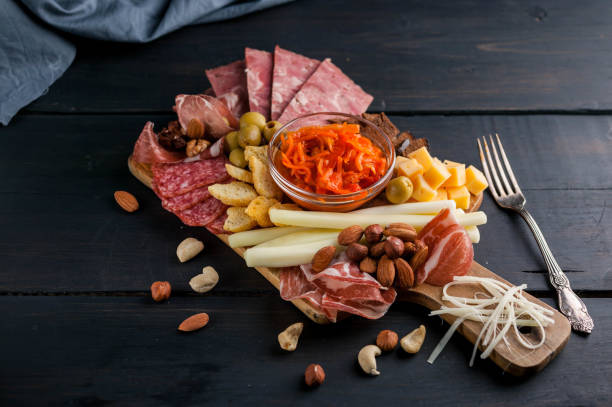 istock Assorted from meat and cheese on a chopping board. Smoked sausage, meat roll from a turkey with cheese, jamon, olives, nuts and various grades of cheese. Low key. Dark wooden background 907944618