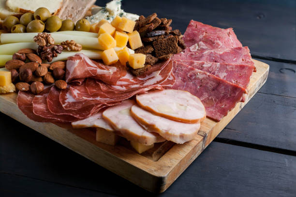 istock Assorted from meat and cheese on a chopping board. Smoked sausage, meat roll from a turkey with cheese, jamon, olives, nuts and various grades of cheese. Low key. Dark wooden background 907945034