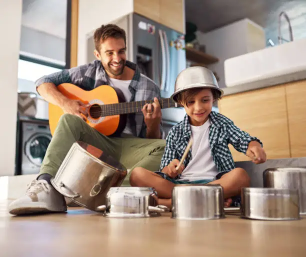 Shot of a happy father accompanying his young son on the guitar while he drums on a set of cooking pots