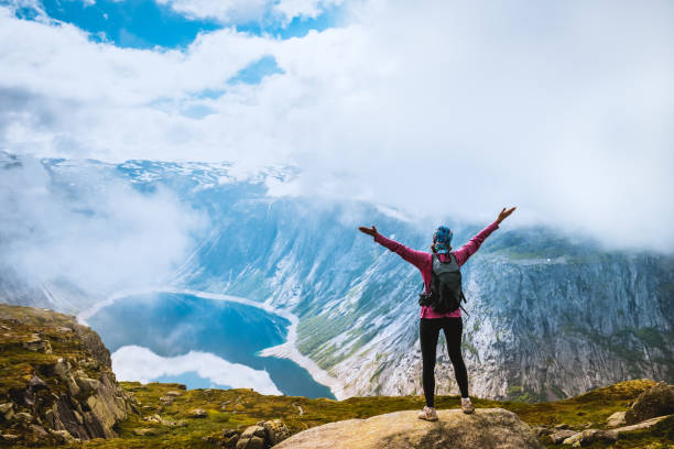 istock Young woman with backpack standing on fjord coast 907950936
