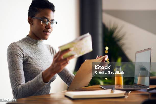 Attractive Young Afro American Businesswoman Receiving From Post Envelope With Documentation For Project Earning Money Online Professional Designer In Eyewear Packing Working Papers For Mailing Stock Photo - Download Image Now