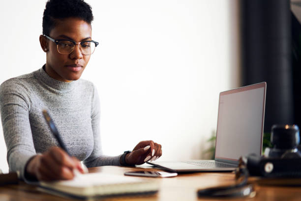 istock Pensive prosperous afro american graphic designer concentrated on creating blueprint drawing sketch, skilled copywriter noting ideas for advertising campaign sitting near laptop with blank screen 907951926