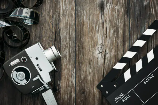 Vintage film camera, filmstrip and clapper board on a wooden desktop, cinema and filmmaking concept