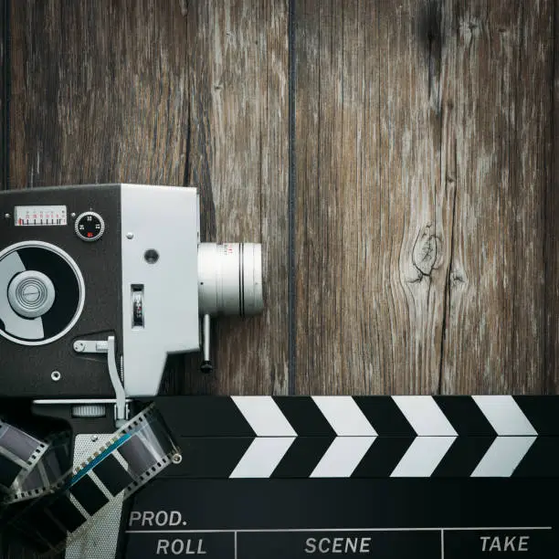 Vintage film camera, filmstrip and clapper board on a wooden desktop, cinema and filmmaking concept