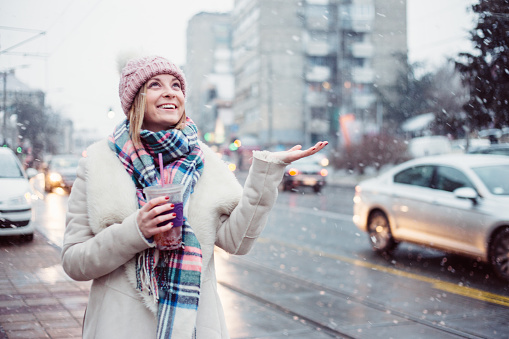 Young women on city street enjoy in snow falling and drinking healthy smoothie