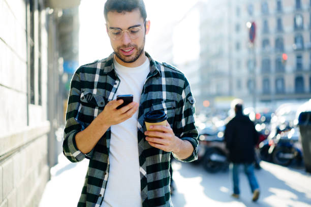 istock Young concentrated student dressed in stylish outfit sending messages to friends using application on cellphone connected to wireless internet.Hipster guy walking at street with smartphone 907954446