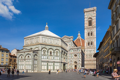 A summer day at Piazza del Duomo (Cathedral Square) in Florence, Italy. The building in the foreground is the Baptistery of St John, one of the oldest buildings in the city. Behind it is the majestic Florence Cathedral (Cattedrale di Santa Maria del Fiore), consecrated in 1436.