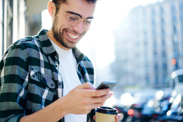 istock Cheerful happy blogger texting funny feedback in website on smartphone using high speed LTE  4G internet while strolling at sunny day on street.Smiling hipster guy reading message on his cellphone 907960720
